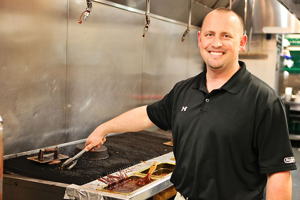 Smiling man grilling food in a kitchen.